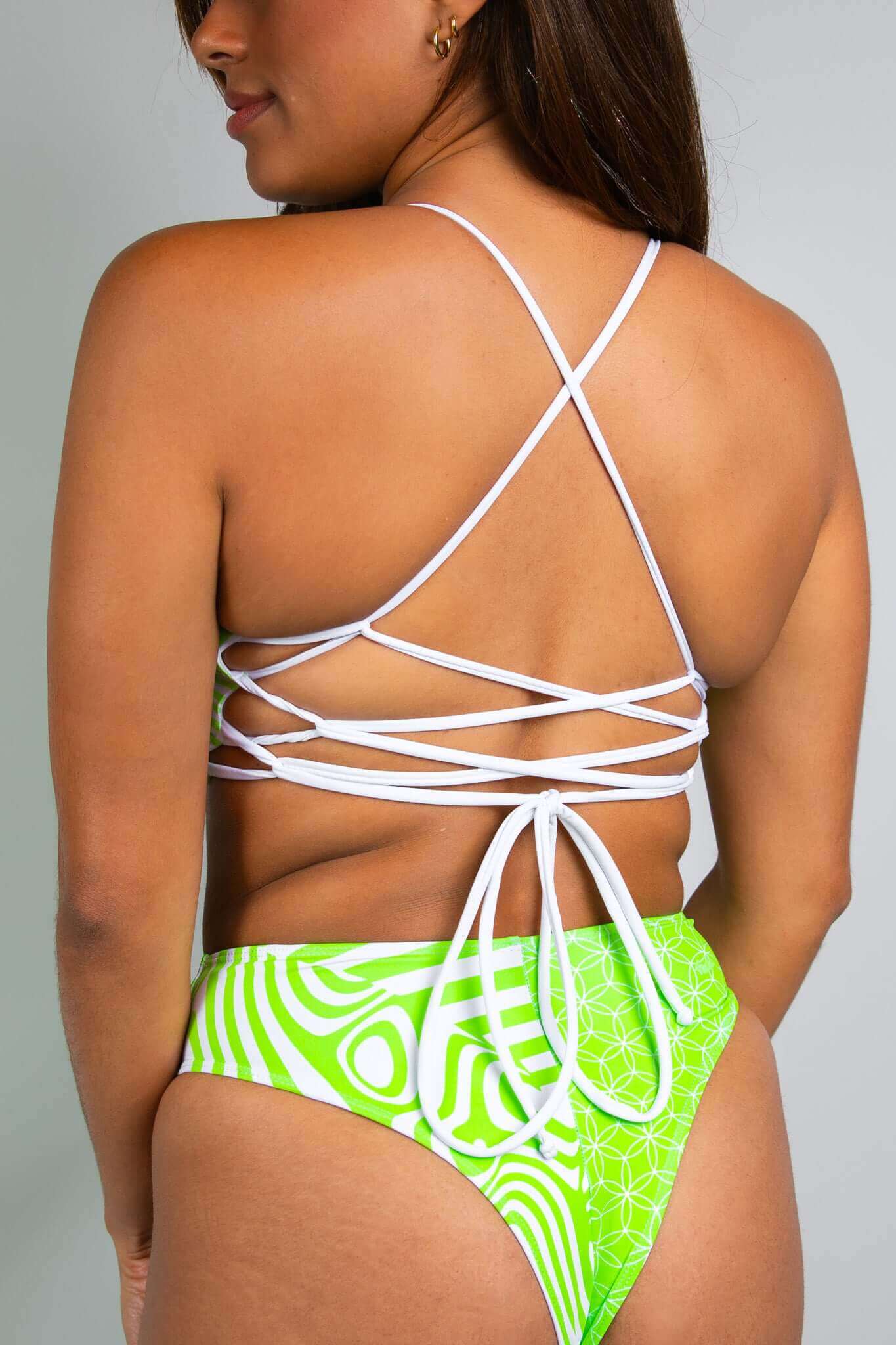 Back view of a woman in a Freedom Rave Wear outfit with green and white psychedelic patterns, featuring crisscross lace-up detail.