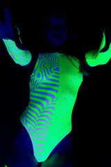 Woman in a Freedom Rave Wear bodysuit glowing under blacklight, featuring green and white patterns with arm sleeves