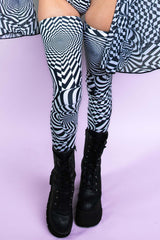 A woman's legs, wearing black boots and black and white geometric leg sleeves that go up to her upper thigh.