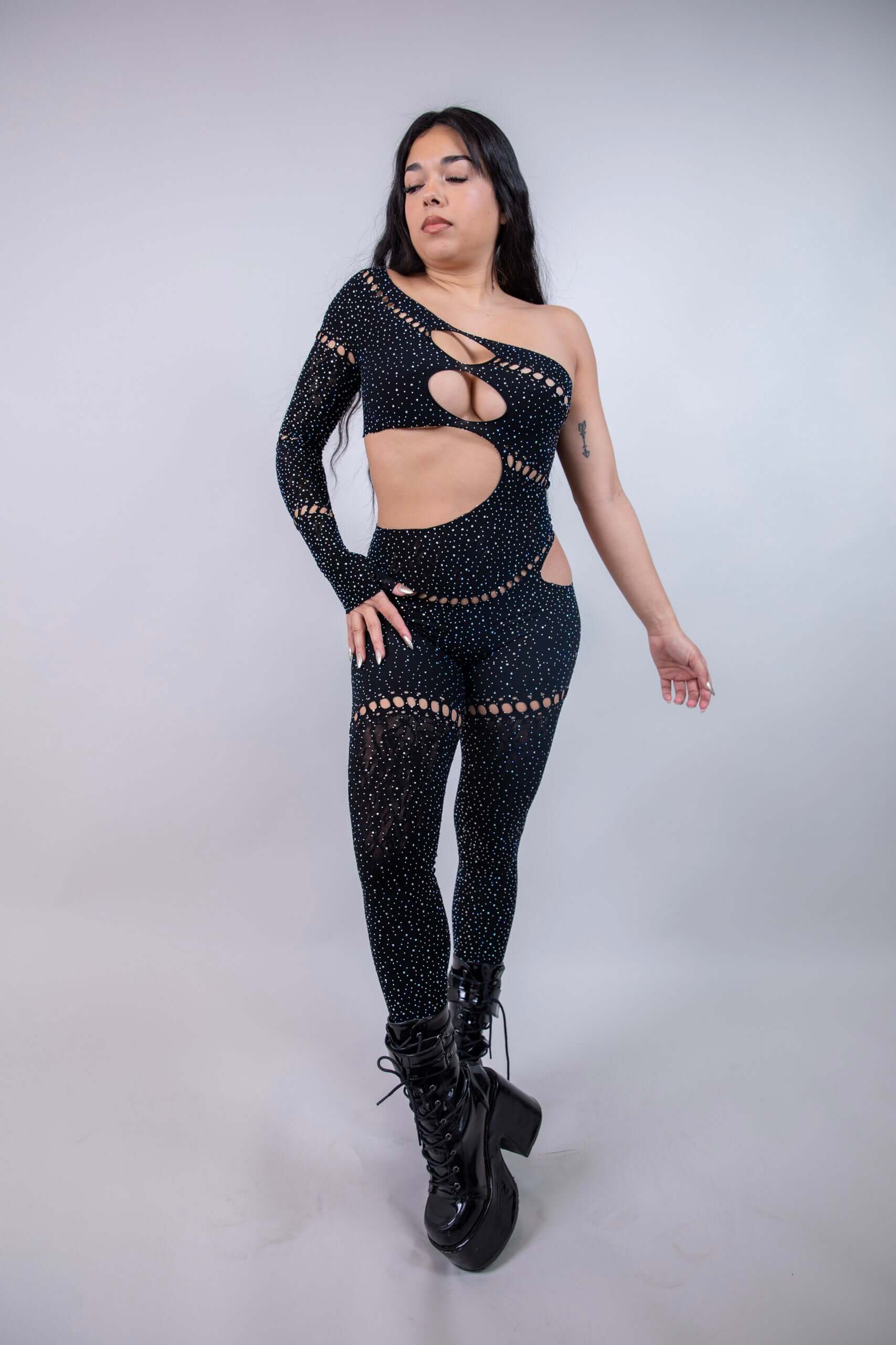 Model wearing The Zoe Asymmetrical Rhinestone Jumpsuit in black, showcasing cutouts and shimmering rhinestones, ideal for rave outfits.