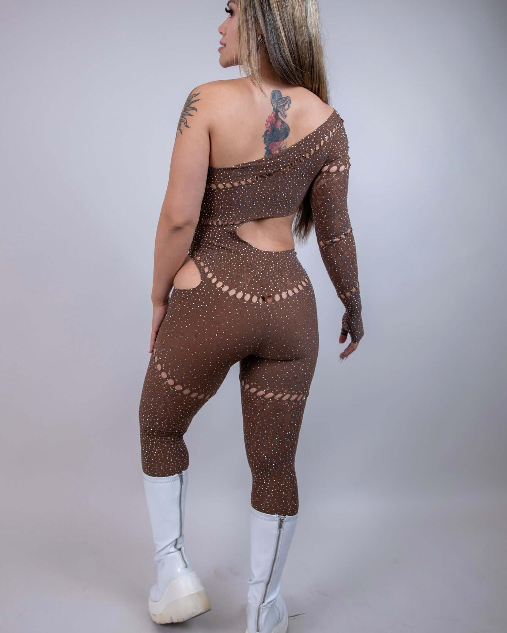 Model showcasing The Zoe Asymmetrical Rhinestone Jumpsuit in brown, featuring cutouts and rhinestones, perfect for rave outfits.