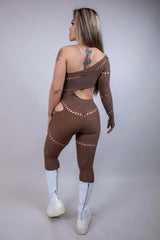 Model showcasing The Zoe Asymmetrical Rhinestone Jumpsuit in brown, featuring cutouts and rhinestones, perfect for rave outfits.