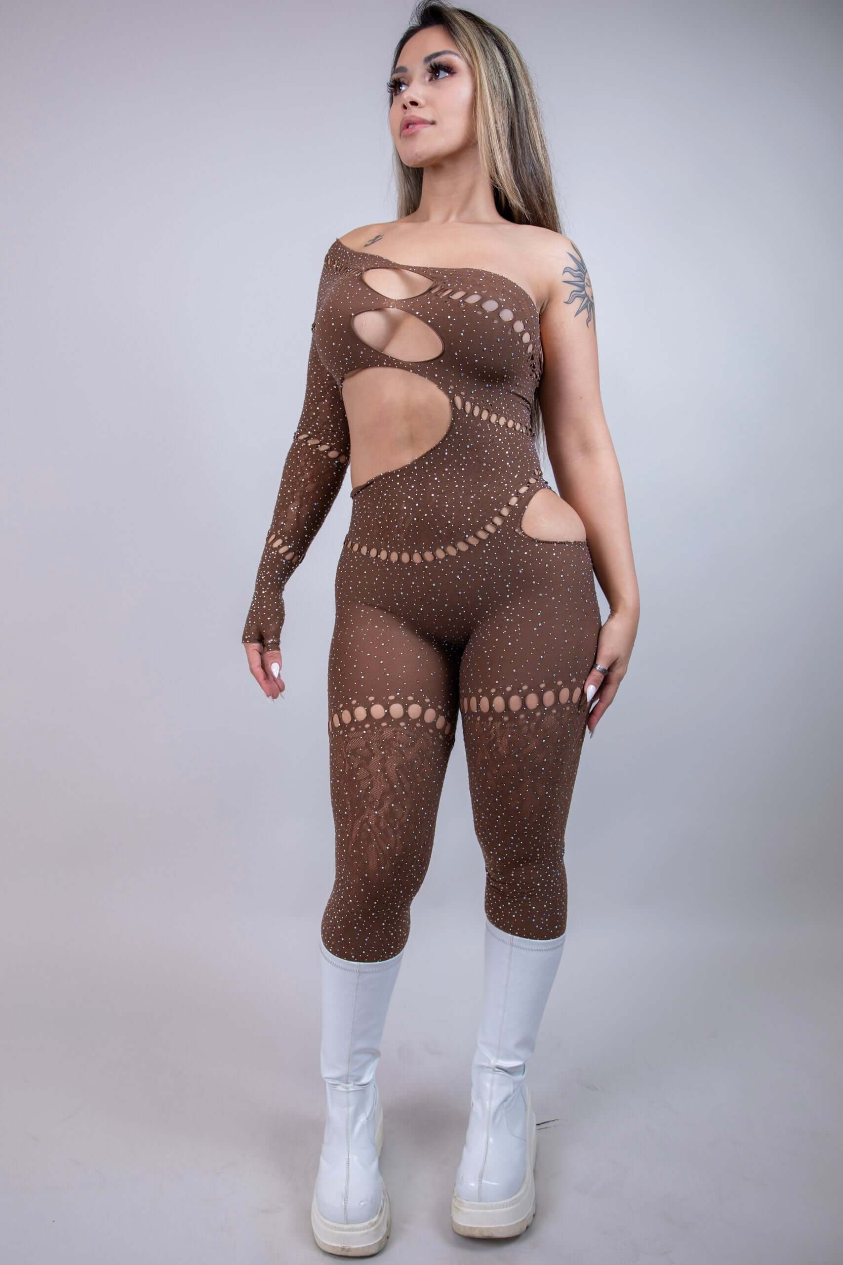 Model wearing The Zoe Asymmetrical Rhinestone Jumpsuit in brown, showcasing cutouts and rhinestones, perfect for rave outfits.