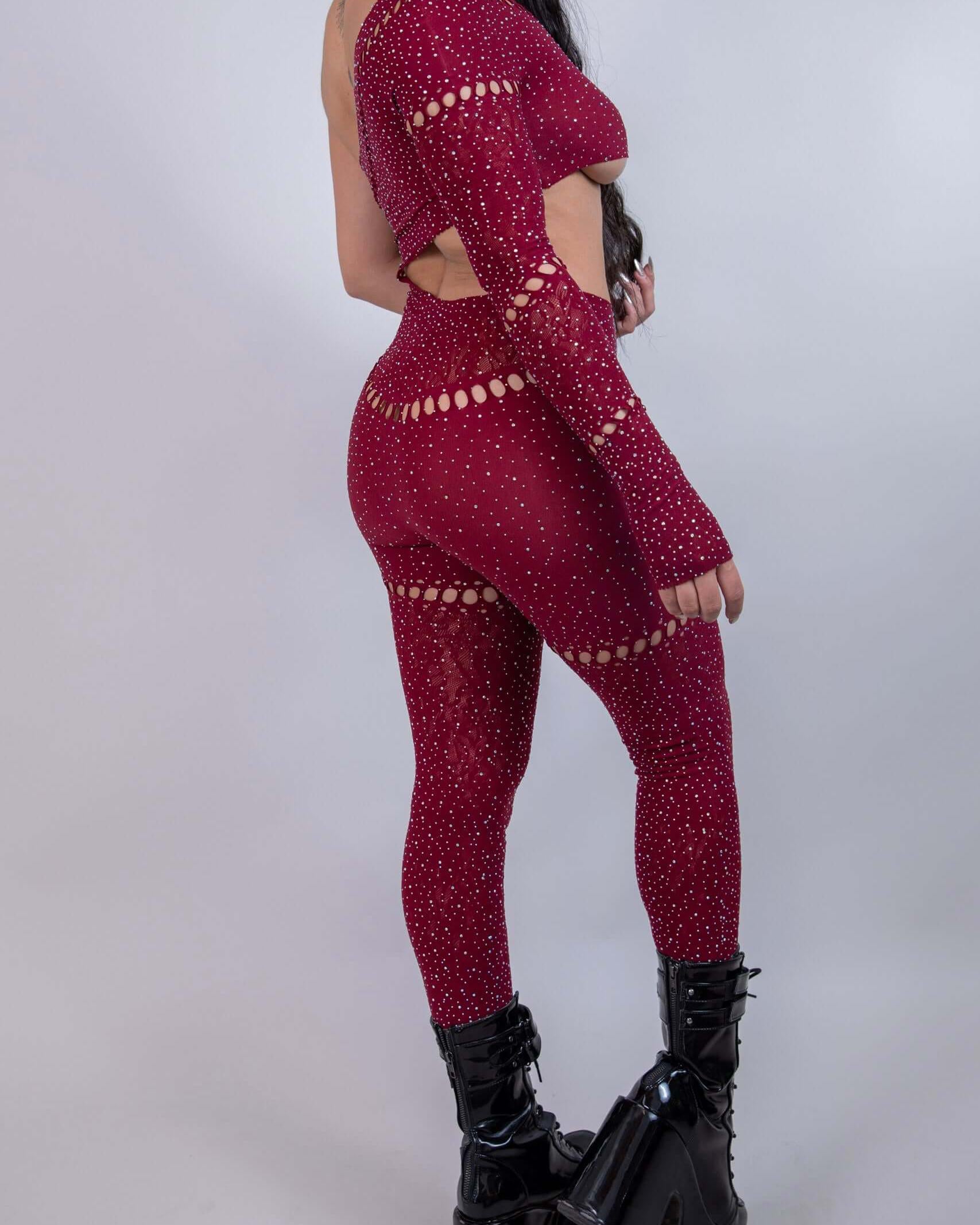 Model showcasing The Zoe Asymmetrical Rhinestone Jumpsuit in burgundy with cutouts and rhinestones, perfect for rave outfits.