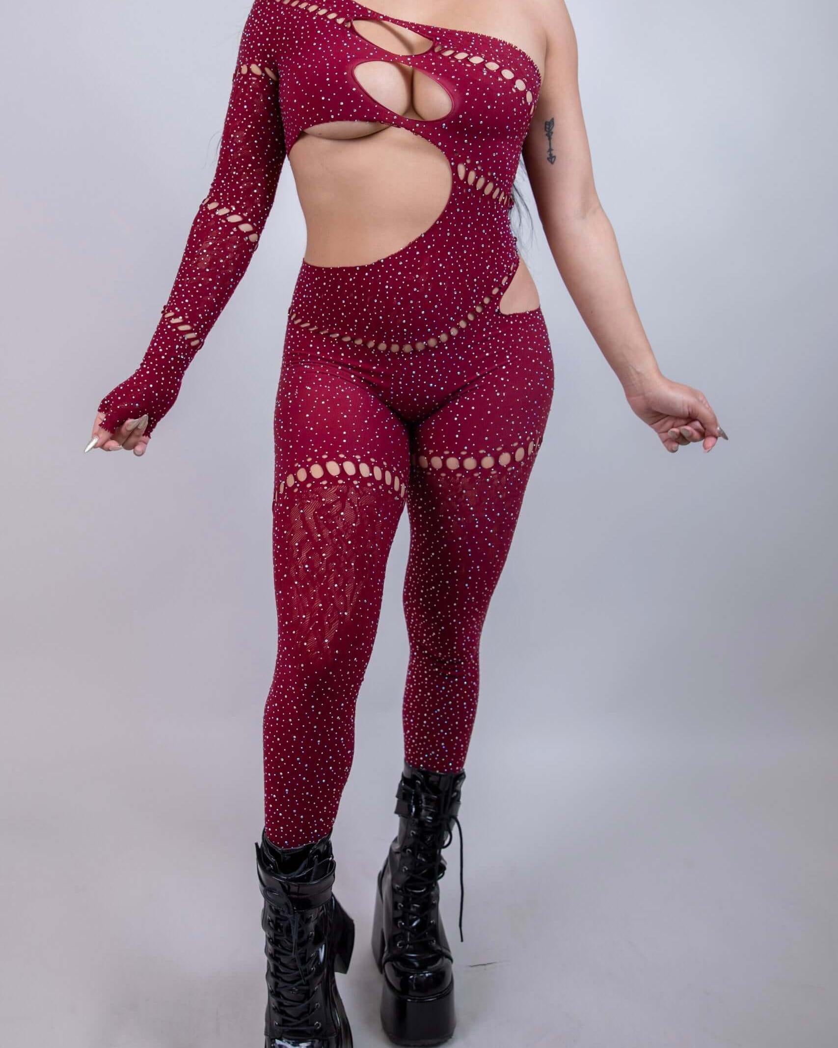 Model wearing The Zoe Asymmetrical Rhinestone Jumpsuit in burgundy, featuring cutouts and rhinestones, perfect for rave outfits.