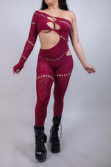 Model wearing The Zoe Asymmetrical Rhinestone Jumpsuit in burgundy, featuring cutouts and rhinestones, perfect for rave outfits.