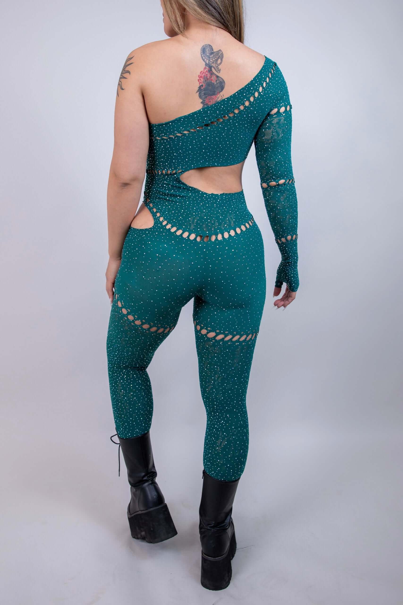 Model showcasing the back of The Zoe Asymmetrical Rhinestone Jumpsuit in emerald, featuring cutouts and rhinestones.