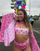 Radiant festival-goer beams in a geometric-patterned wisteria rave outfit with plush ears and whimsical makeup, capturing the lively spirit of the music festival
