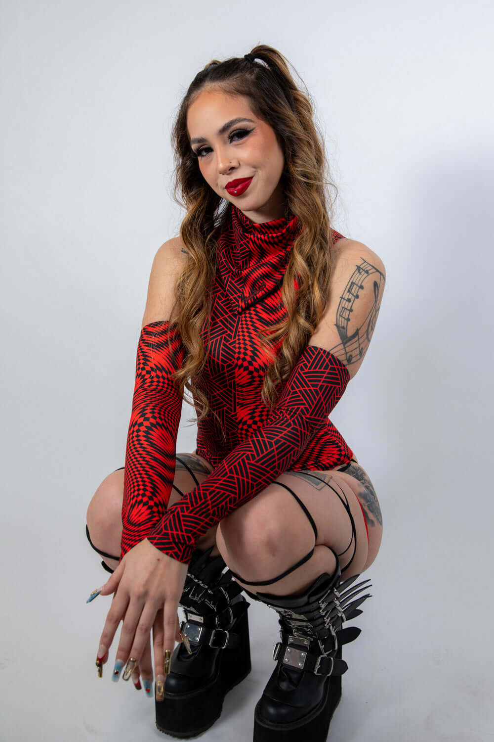 Model showcasing Amplitude Arm Sleeves in red and black, styled with rave outfits and trendy accessories.
