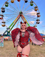 Festival-goer in a striking red and black abstract-patterned rave outfit with mesh details, standing boldly in front of a Ferris wheel, embodying the vibrant spirit of music festivals.