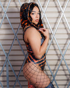Model wearing Atomic Assassin Hood in orange and black, showcasing post-apocalyptic style with netted leggings against industrial backdrop.