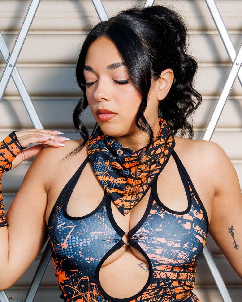 Woman wearing Atomic Bandana in orange and black with post-apocalyptic design, styled as a neck scarf for festival fashion.