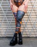 Woman wearing Atomic Leg Sleeves with vibrant patterns, standing against a metal gate, showcasing bold, high-energy design.