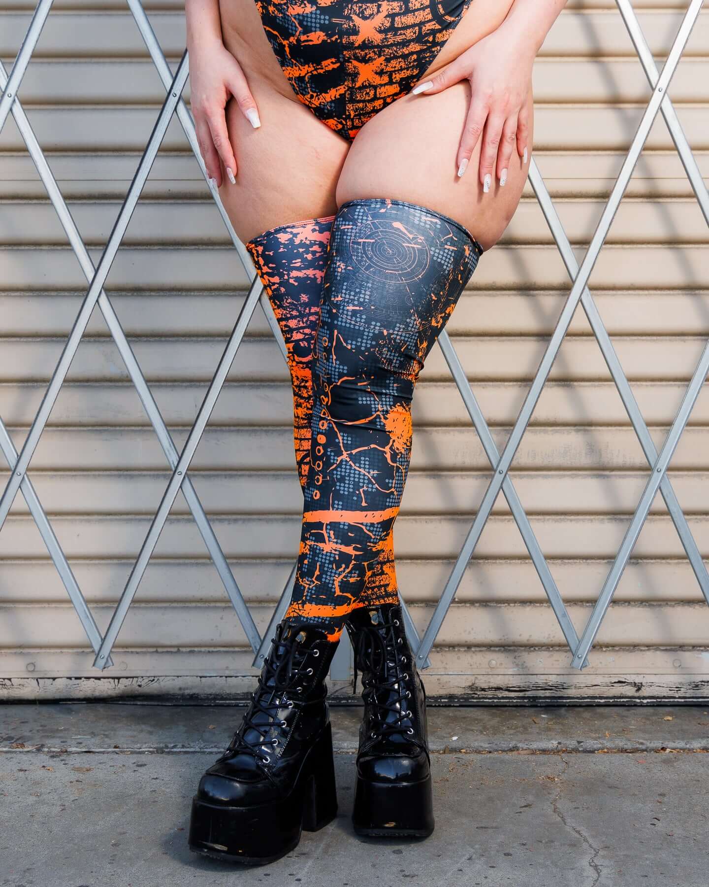 Woman wearing Atomic Leg Sleeves with vibrant patterns, standing against a metal gate, showcasing bold, high-energy design.