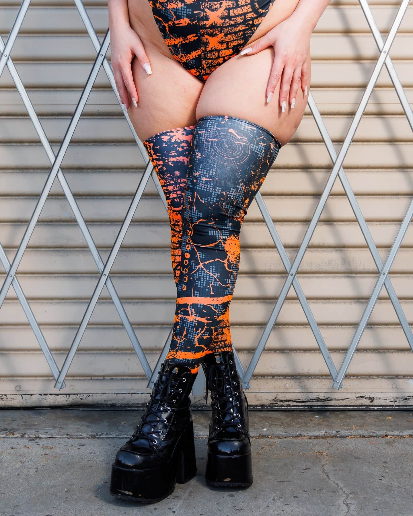 Woman wearing Atomic Leg Sleeves with vibrant patterns, standing against a metal gate, showcasing bold, high-energy design.