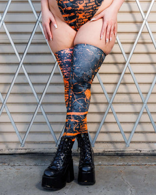 Woman wearing Atomic Leg Sleeves with vibrant patterns, standing against a metal gate, showcasing bold, high-energy design.