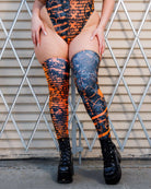 Model wearing Atomic Leg Sleeves with vibrant patterns and high-energy design, paired with black platform boots against a metal backdrop.