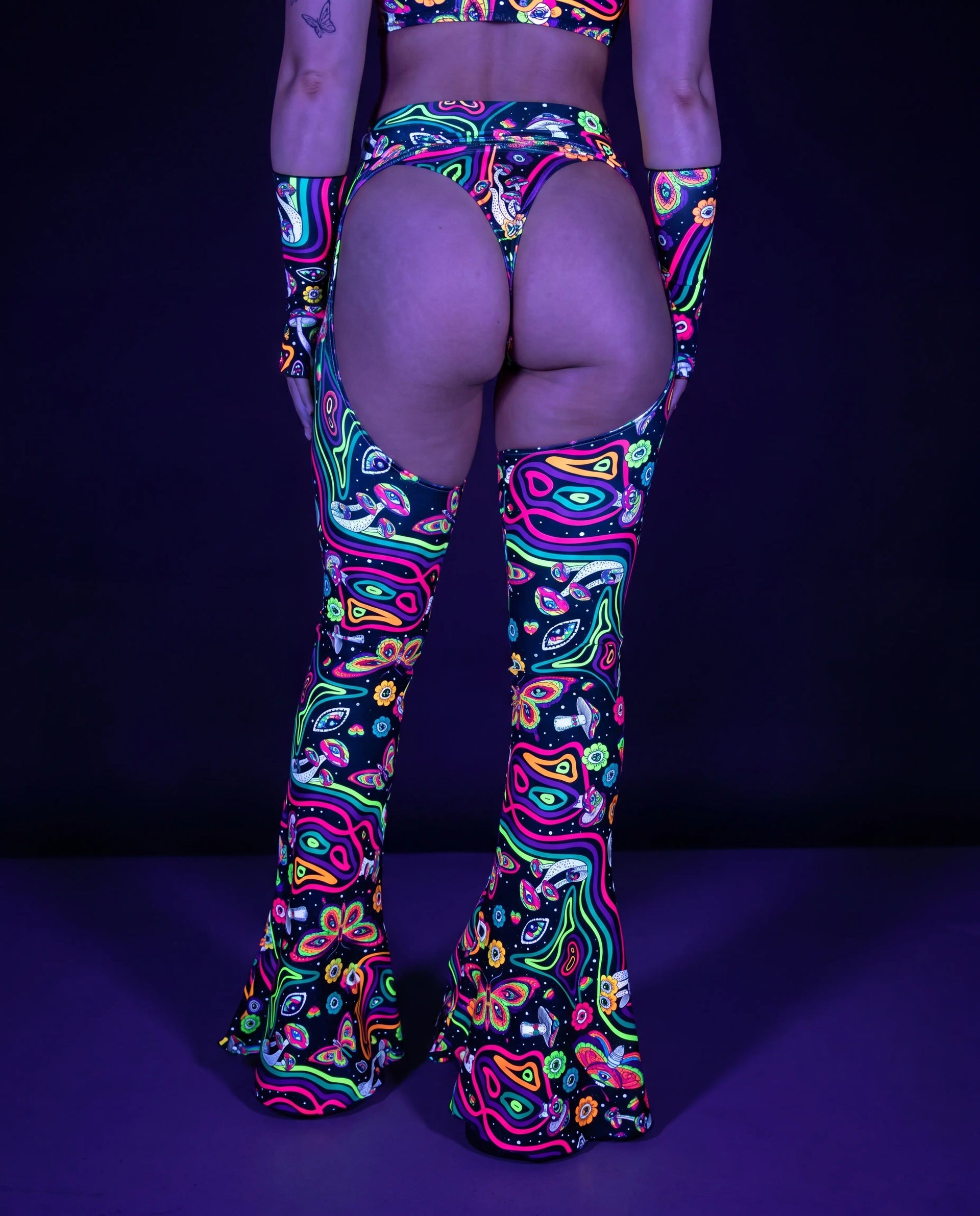 Awaken Bell Chaps from the back, featuring a vibrant psychedelic pattern with mushrooms and eyes, perfect for a rave festival. — uv