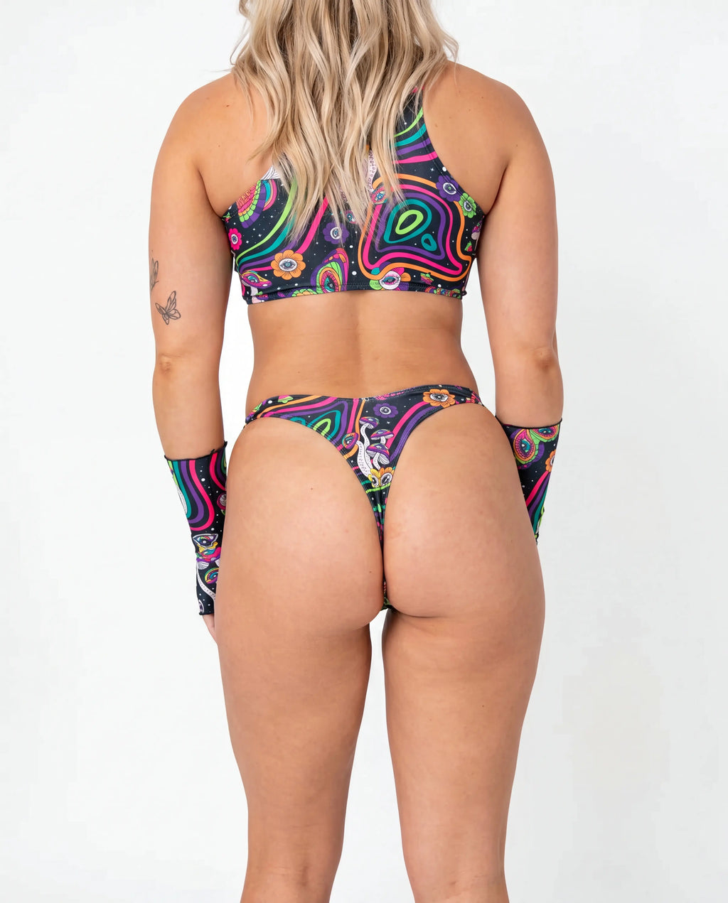 Awaken Risk Bottoms front view, featuring a model in black high-cut rave bottoms with a vibrant psychedelic mushroom and eye pattern, perfect for festivals. — cyc_2