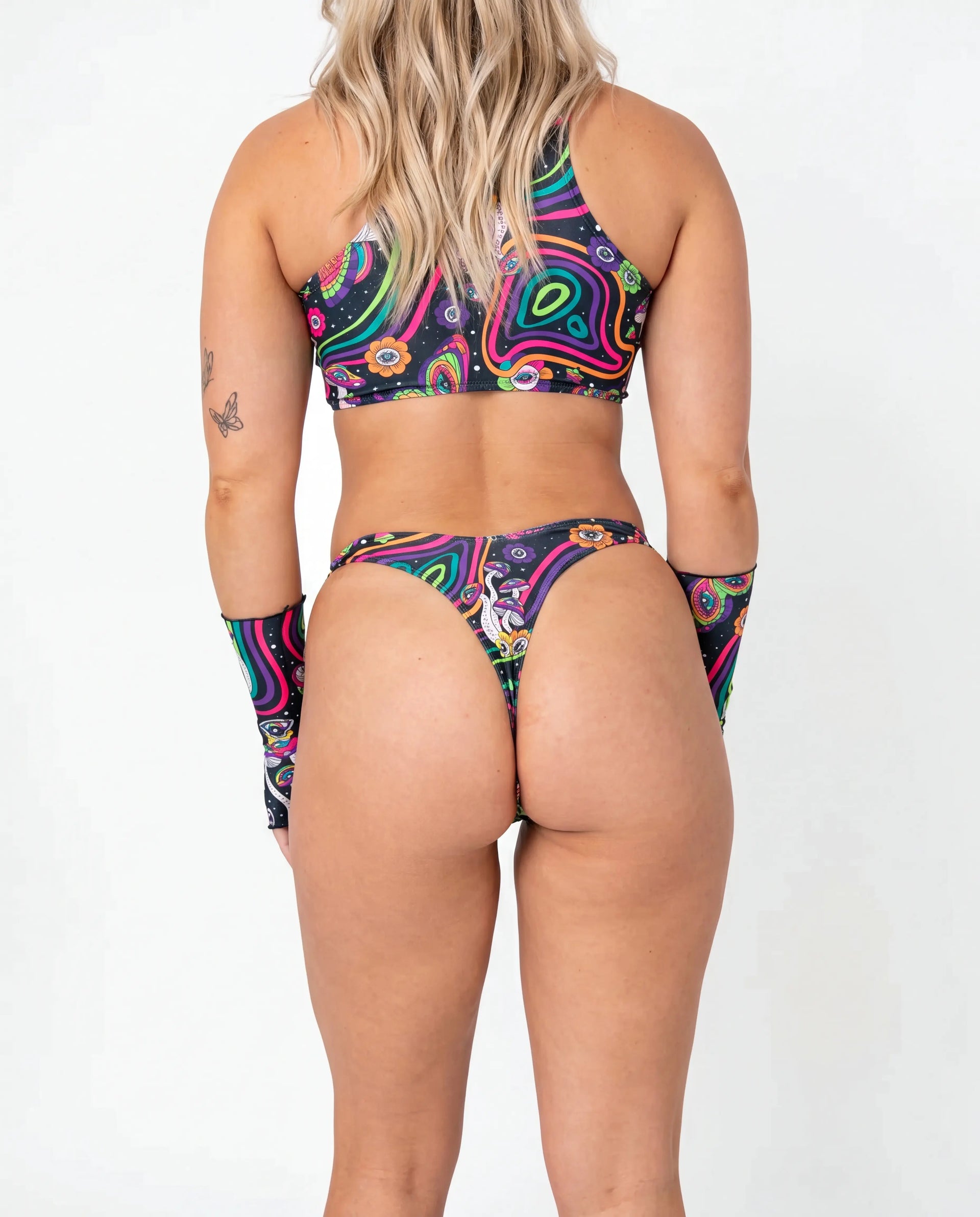 Awaken Risk Bottoms front view, featuring a model in black high-cut rave bottoms with a vibrant psychedelic mushroom and eye pattern, perfect for festivals. — cyc_2