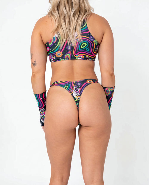 Awaken Risk Bottoms front view, featuring a model in black high-cut rave bottoms with a vibrant psychedelic mushroom and eye pattern, perfect for festivals. — cyc_2