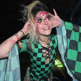 Ecstatic raver in green checkered rave outfit with bold face paint smiles widely, expressing playful festival joy