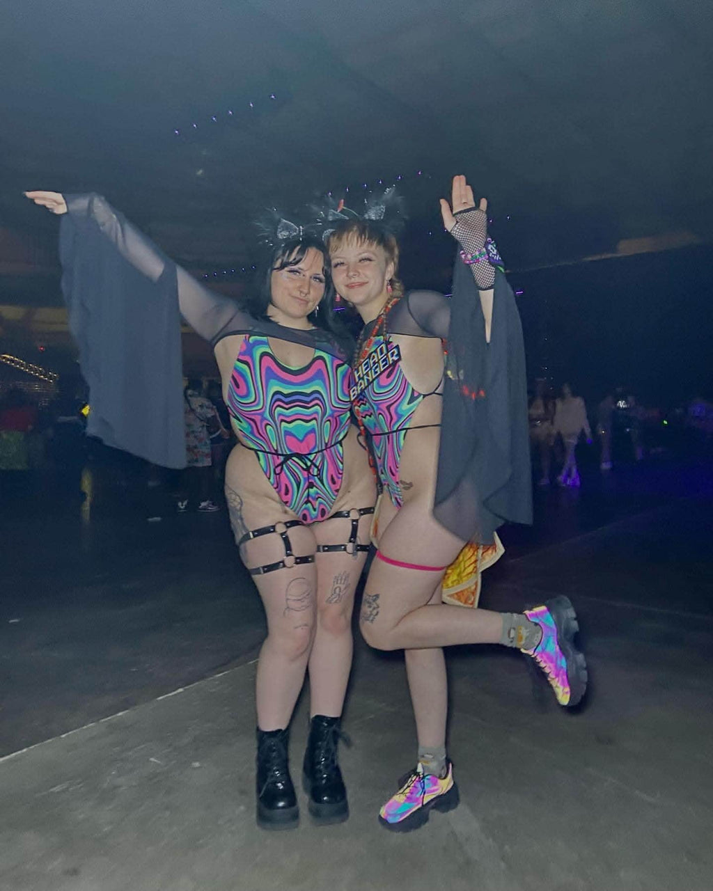 Two friends in vibrant rave outfits, showcasing dramatic bell sleeves and playful poses at a lively event.