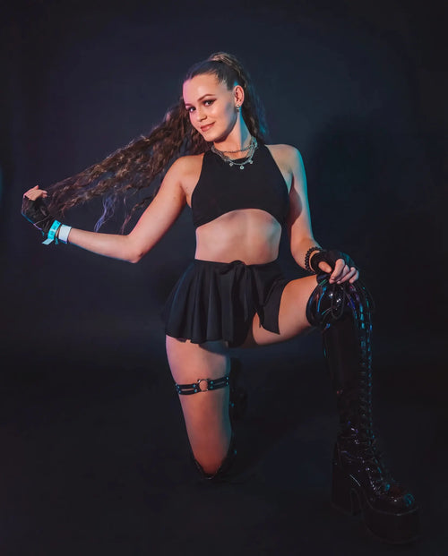 Model wearing black mesh swirl rave skirt with crop top at festival with neon lighting