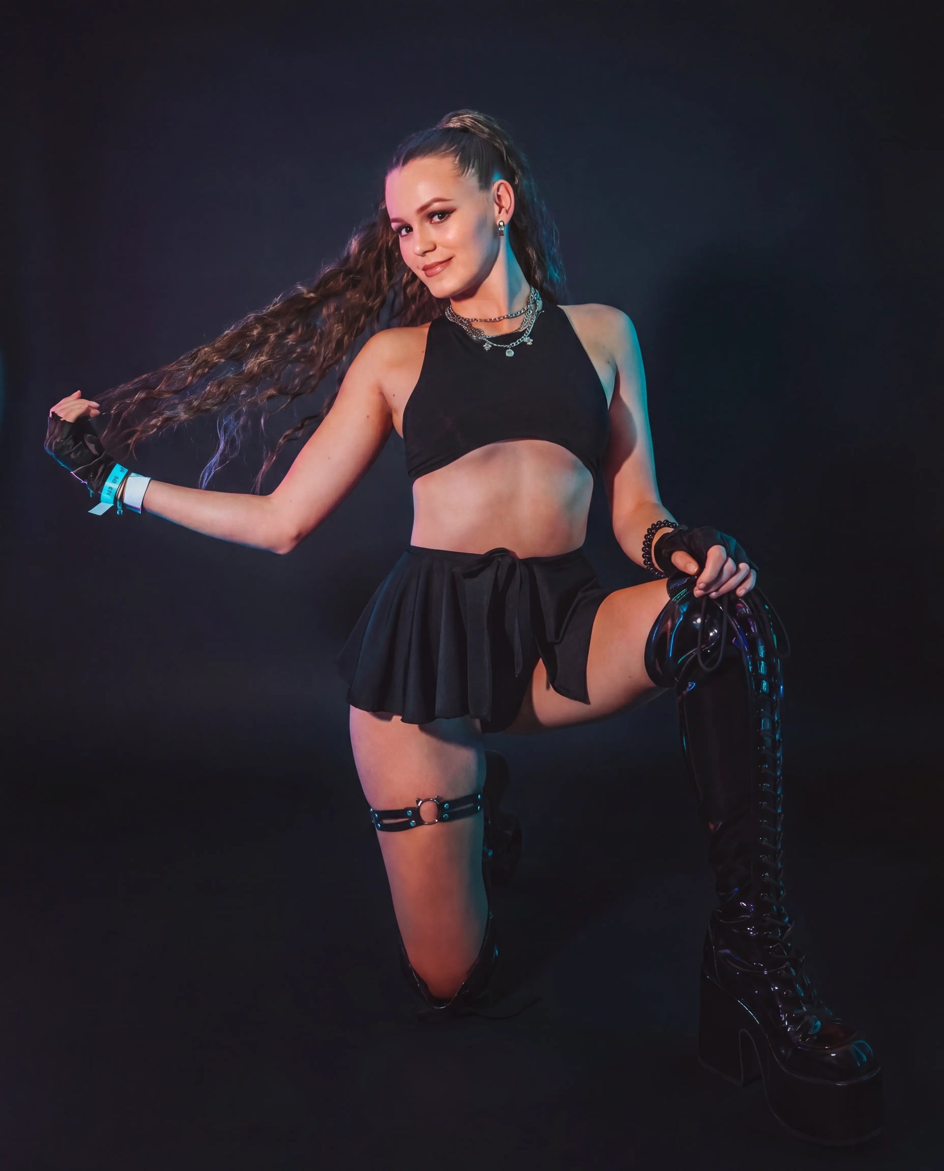 Model wearing black mesh swirl rave skirt with crop top at festival with neon lighting