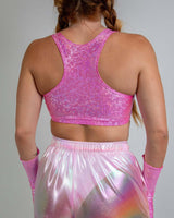 Back view of a model wearing a pink holographic crop top and shiny pastel pants, perfect for rave outfits.