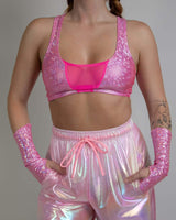 Model wearing a pink holographic top and shiny trousers, showcasing a vibrant rave outfit with mesh details.