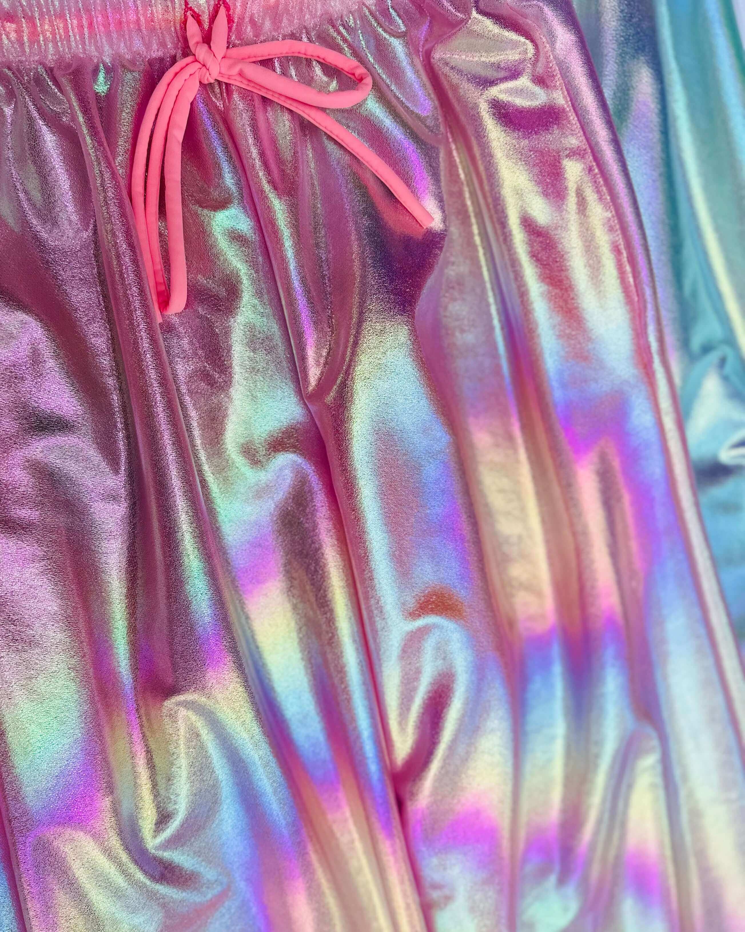 Iridescent pink Bubble Gum Lucy Pants close-up, showcasing the shiny fabric and drawstring details, perfect for rave outfits.