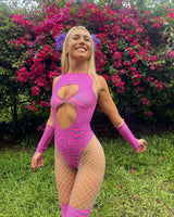 Model in a vibrant pink Cheshire Keyhole Bodysuit with side cutouts, posing against blooming flowers, perfect for rave outfits.