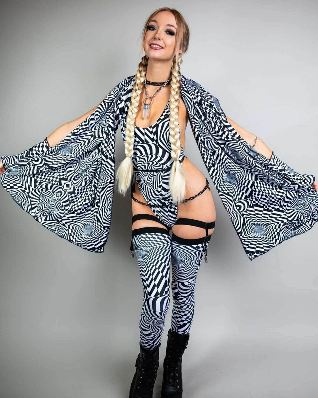 Woman in black and white patterned outfit striking a pose, showcasing a stylish rave look with bold accessories.