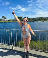 Freedom Rave Wear outfit with black and white optical illusion design, paired with fishnet leggings and white sunglasses, worn by a woman by the water.