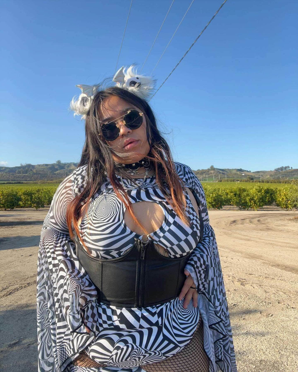 Woman in a striking black and white striped outfit showcasing a bold rave style, complete with accessories in a scenic outdoor setting.