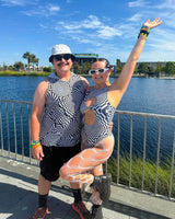 Two friends posing by a waterfront in matching abstract black and white rave outfits, showcasing unique fashion styles.
