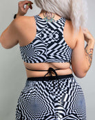 Woman showcasing the back of a Distortion Teaser Top, featuring abstract optical design and crisscross straps for rave outfits.