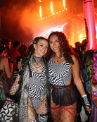 Two friends in abstract optical bodysuits at a vibrant rave, showcasing bold style and energy in the crowd.