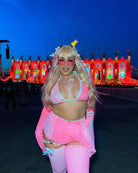 Person in neon pink wrap bikini top enjoying a rave with vibrant lights in the background, showcasing festival fashion.