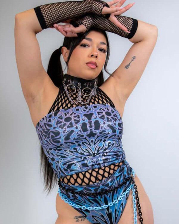 Model showcasing black fishnet arm sleeves as part of a vibrant rave outfit, posing confidently for the camera.