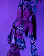 Model wearing Flutter holographic butterfly rave bodysuit in dynamic pose under purple festival lighting
