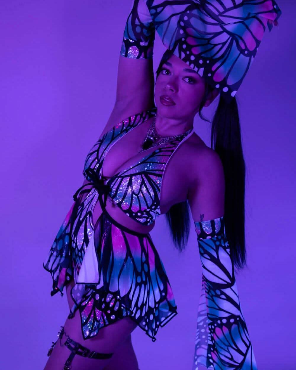 Model wearing Flutter holographic butterfly rave bodysuit in dynamic pose under purple festival lighting