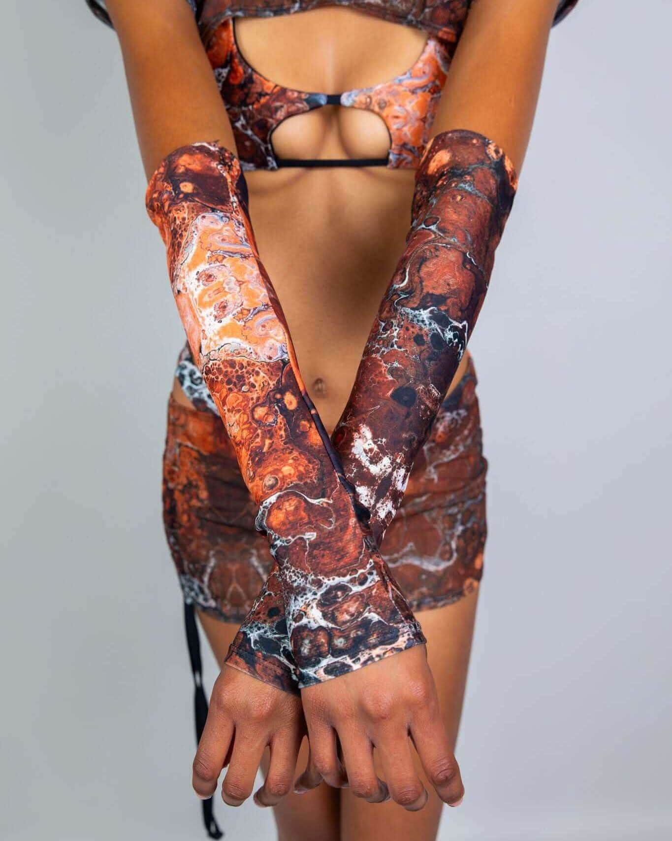 Model wearing Fossil rave arm sleeves in earthy brown marbled pattern, arms crossed showing full coverage