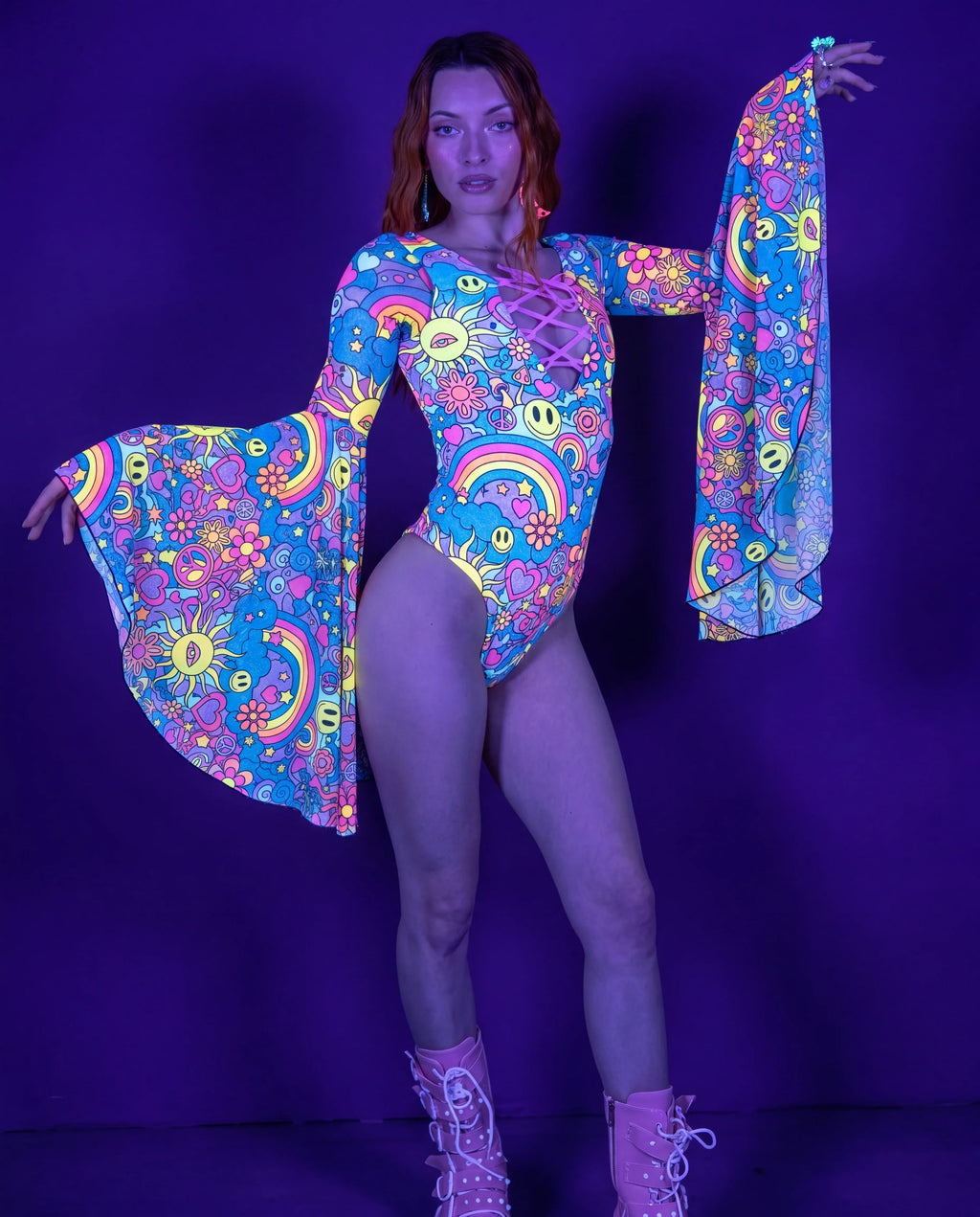 Groovy Goddess Bodysuit front view, featuring a model in a vibrant psychedelic rave bodysuit with bell sleeves and lace-up detail. — UV blacklight