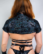 Woman showing back of stylish black crop top with intricate pattern and cut-out straps, perfect for rave outfits.