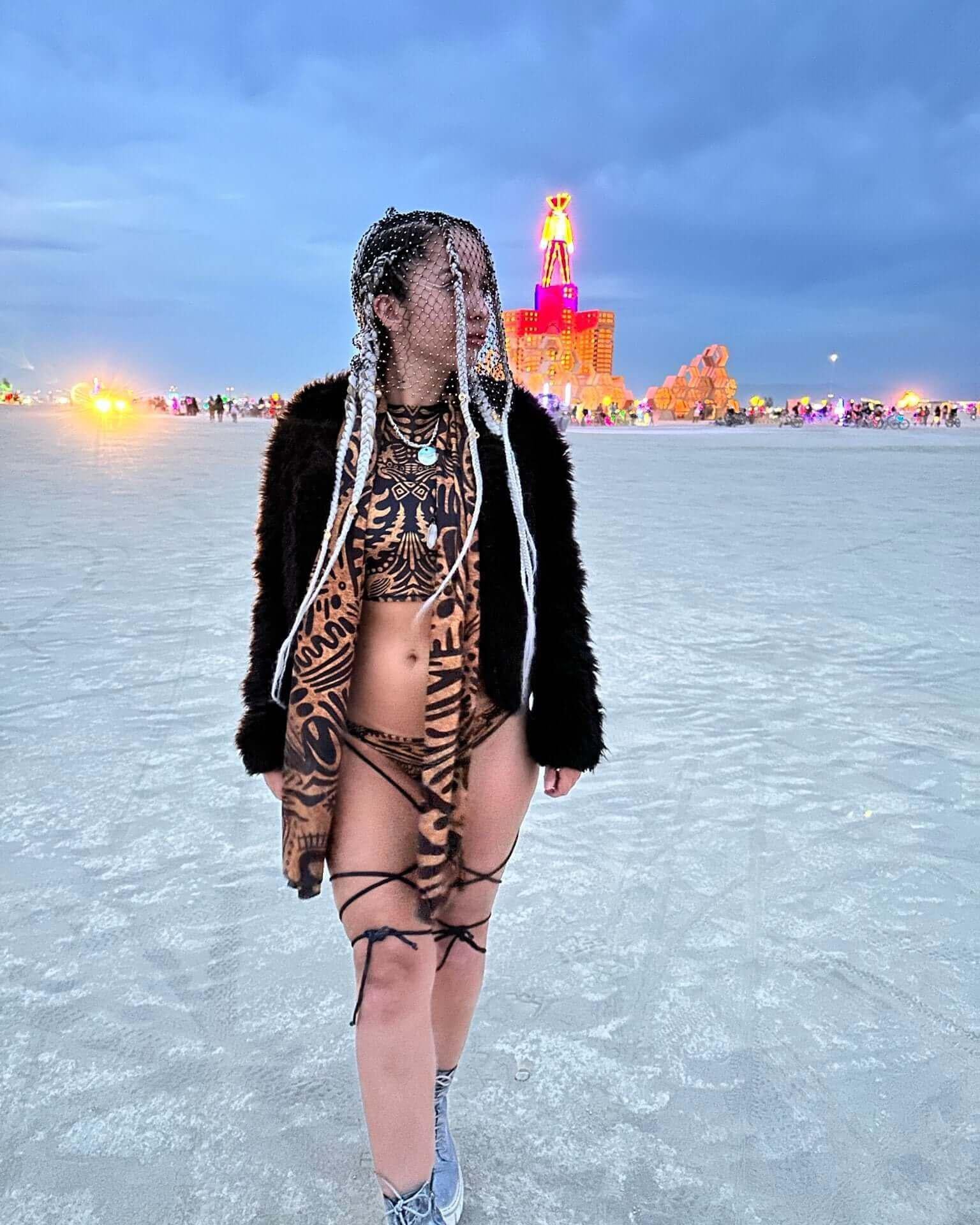 Model in strappy black and animal print bikini at a rave, showcasing a bold festival look against a desert backdrop.