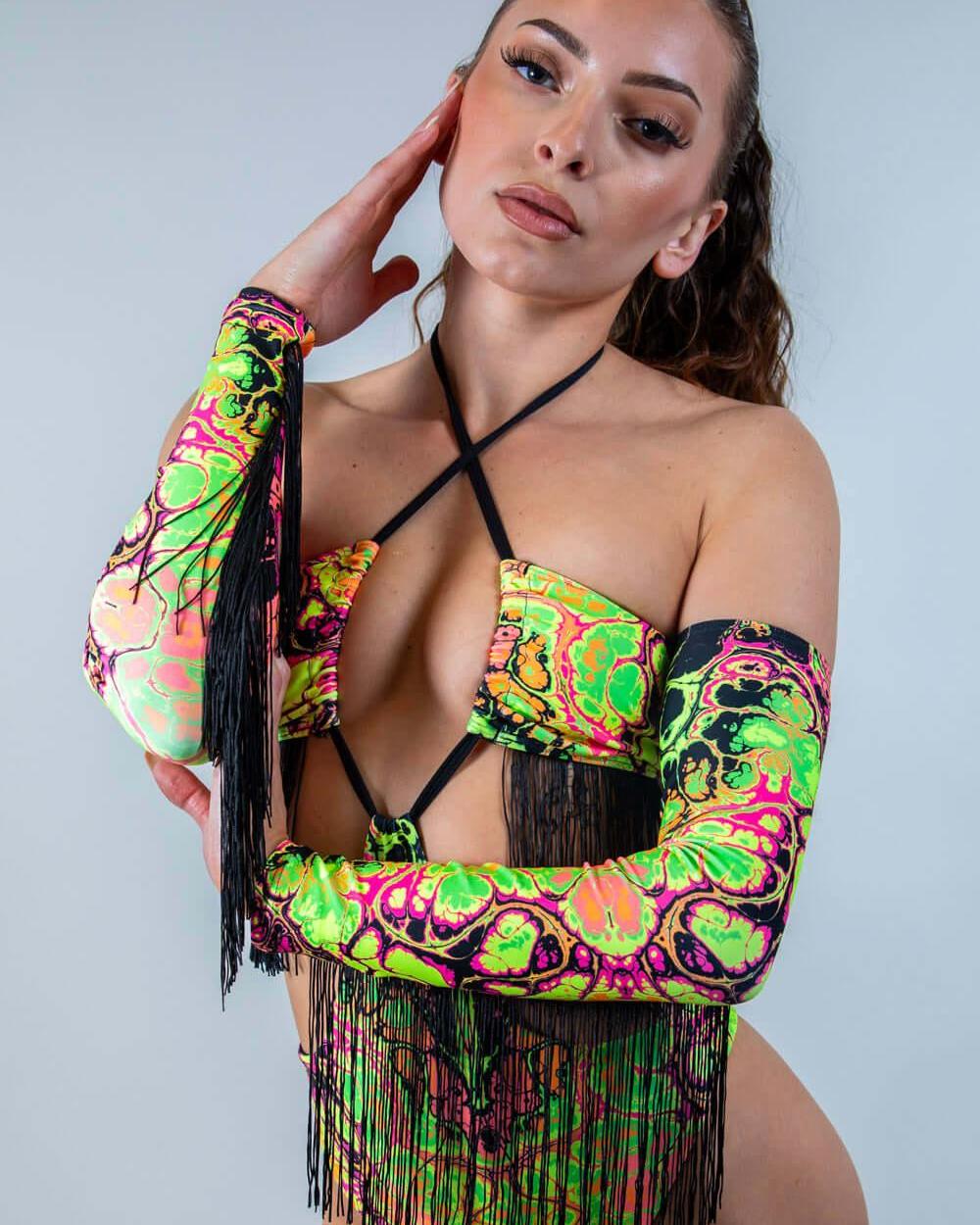 Model wearing vibrant Intensity Arm Sleeves with Fringe, showcasing bold UV patterns and playful black fringe.
