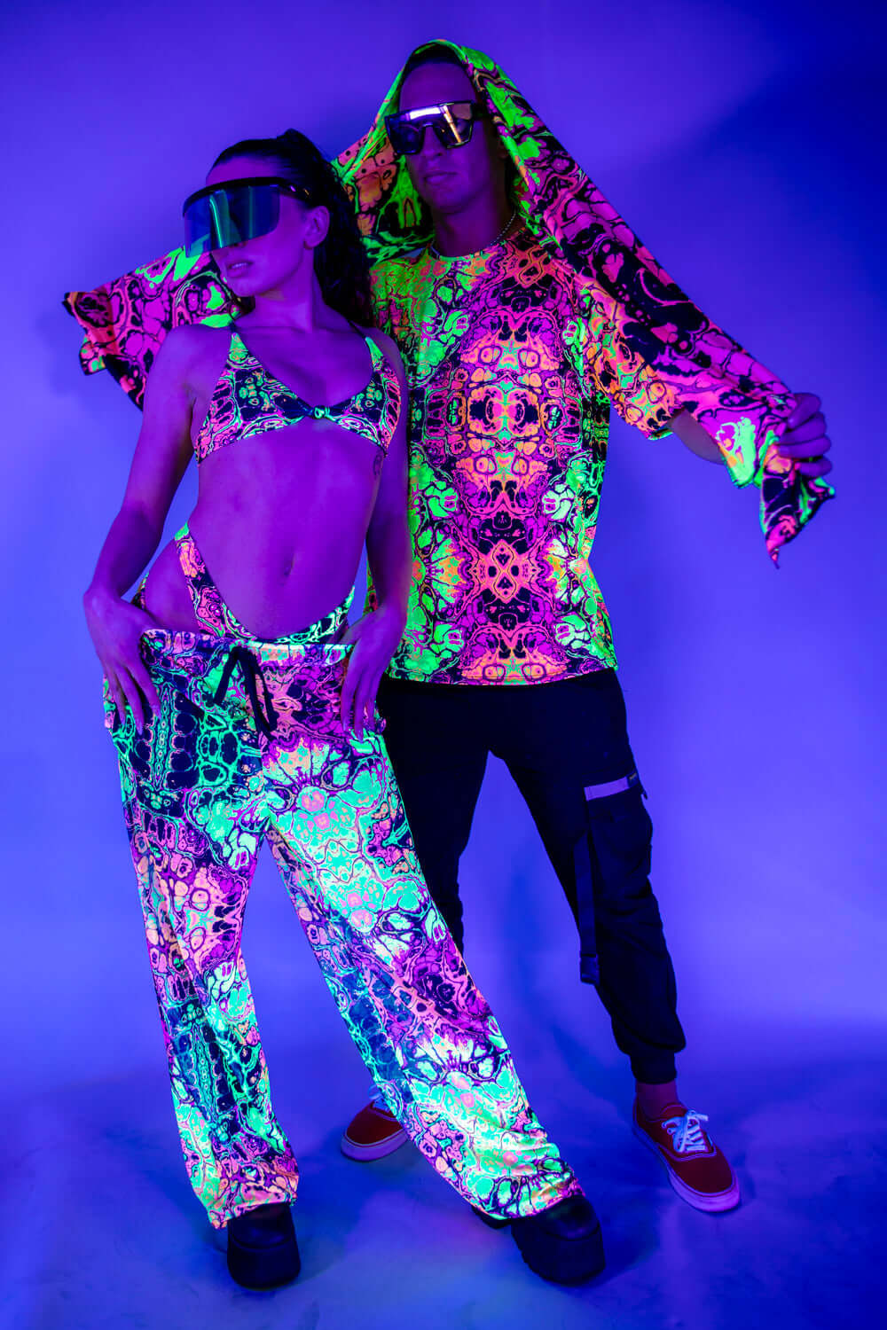 Couple in vibrant neon rave outfits posing under UV light, showcasing colorful festival fashion and accessories.