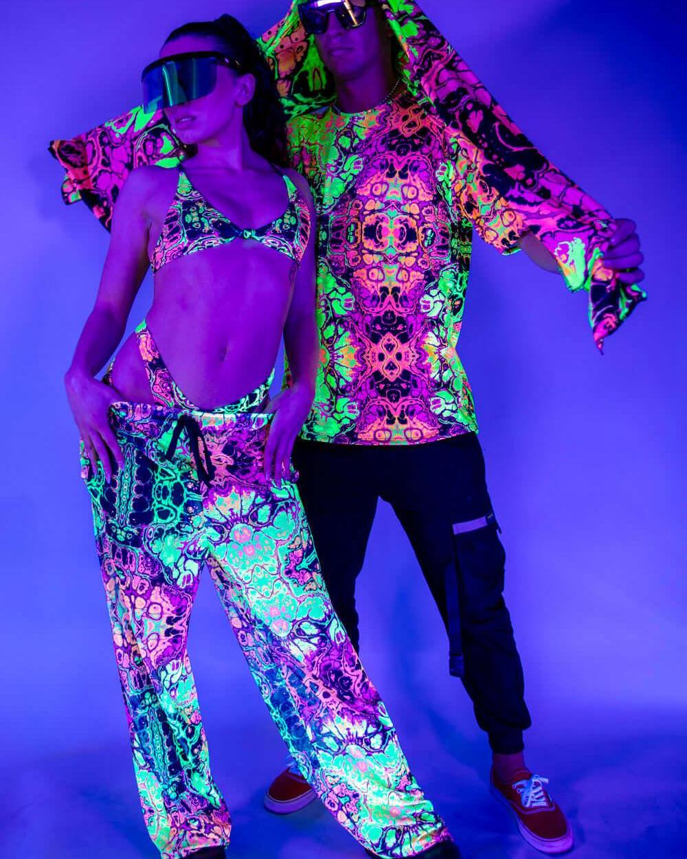 Couple in vibrant neon rave outfits posing under UV light, showcasing colorful festival fashion and accessories.